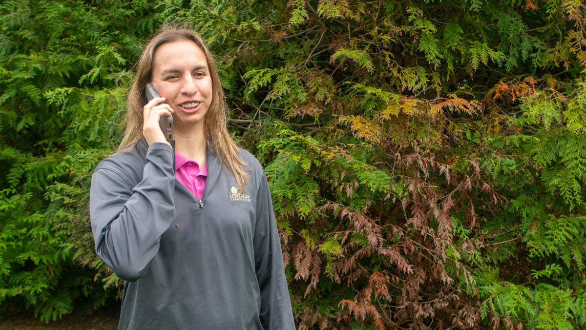 landscape technician on phone in front of shrubs