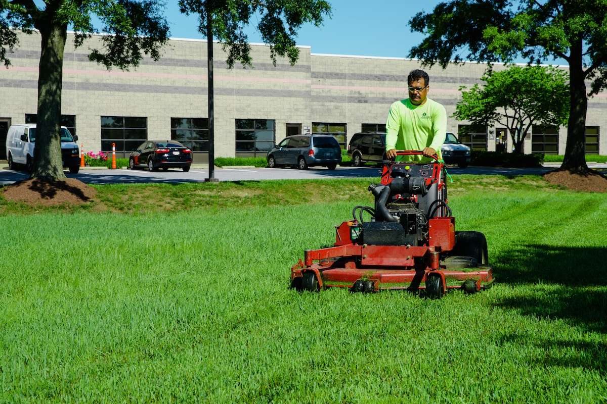 landscape maintenance crew mowing grass lawn near parking lot